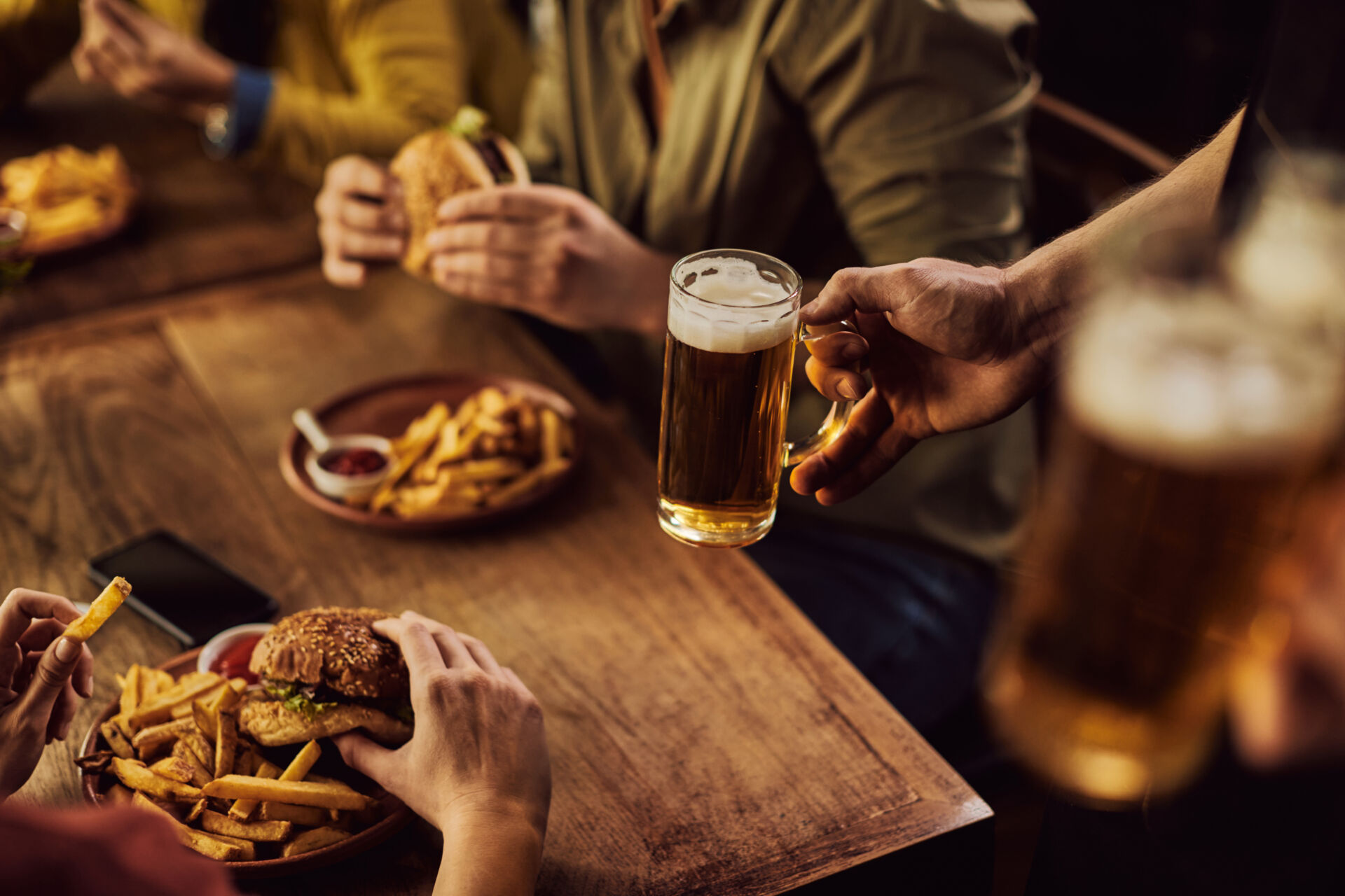 Close-up of waiter serving beer to customers who are eating in a pub.