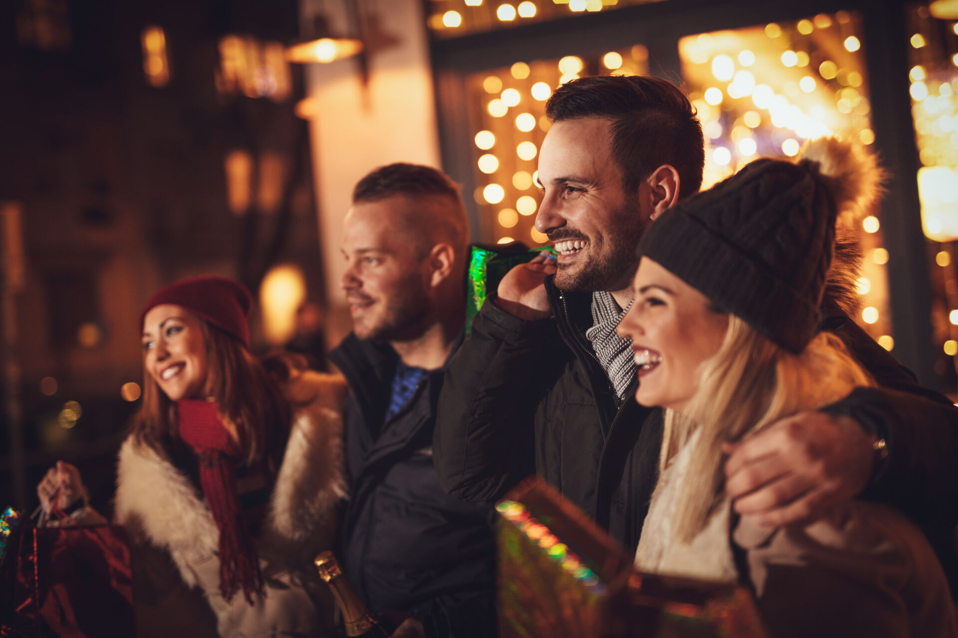 Three young cheerful couple having fun at the Christmas night in the city street with a lot of lights on background.