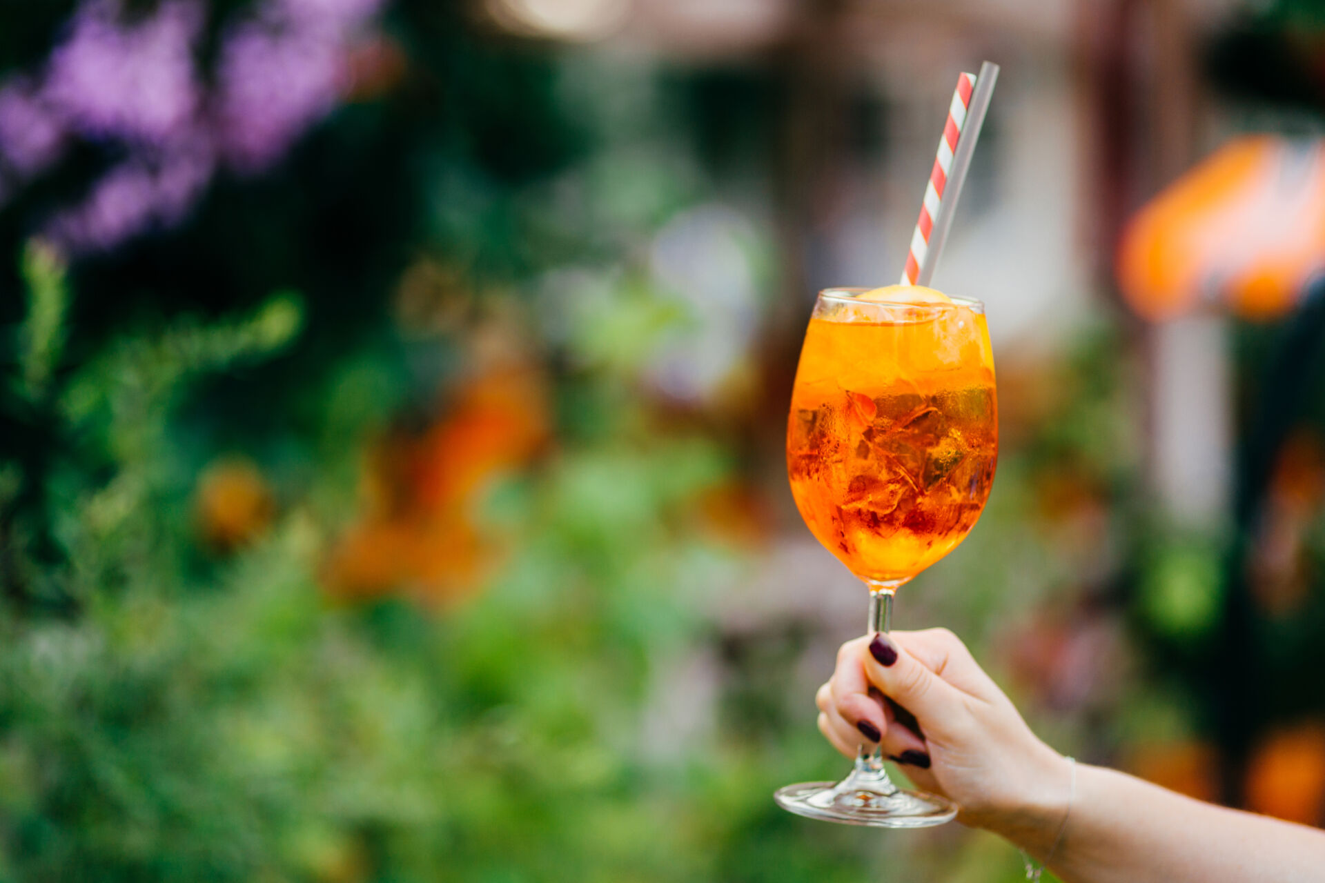 Fresh cocktail in wine glass outdoor against blurred background. Woman holds summer cold drink with ice. Horizontal shot. Tasty acoholic beverage